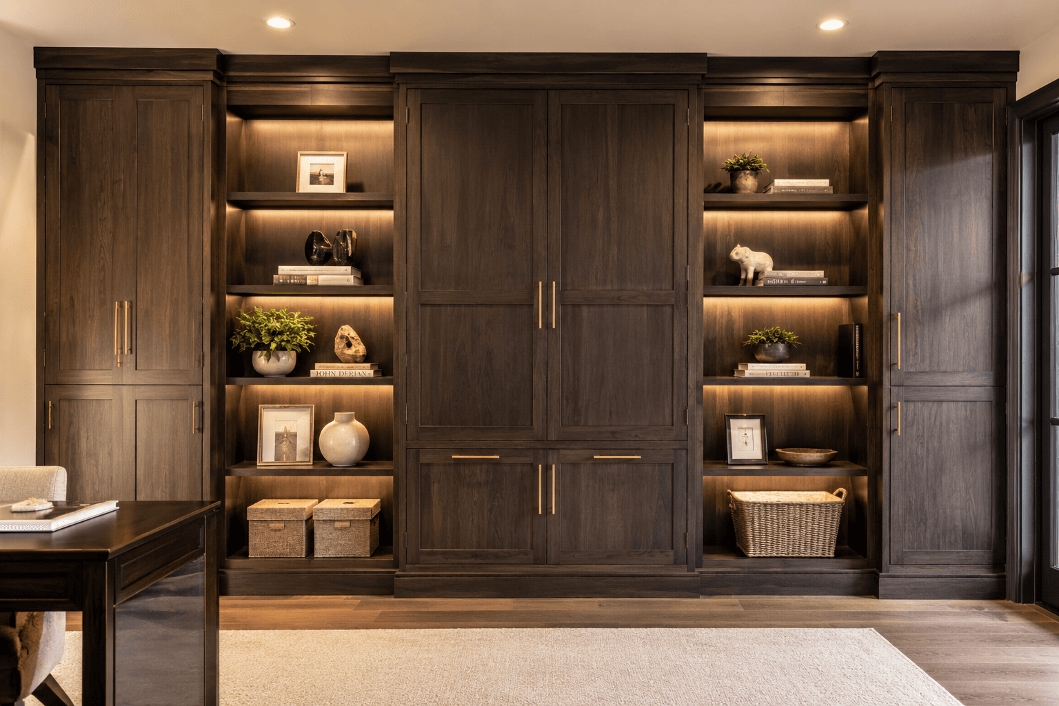 Floor-to-ceiling dark walnut built-in cabinet wall with brass hardware and LED lighting by Benito Fine Carpentry
