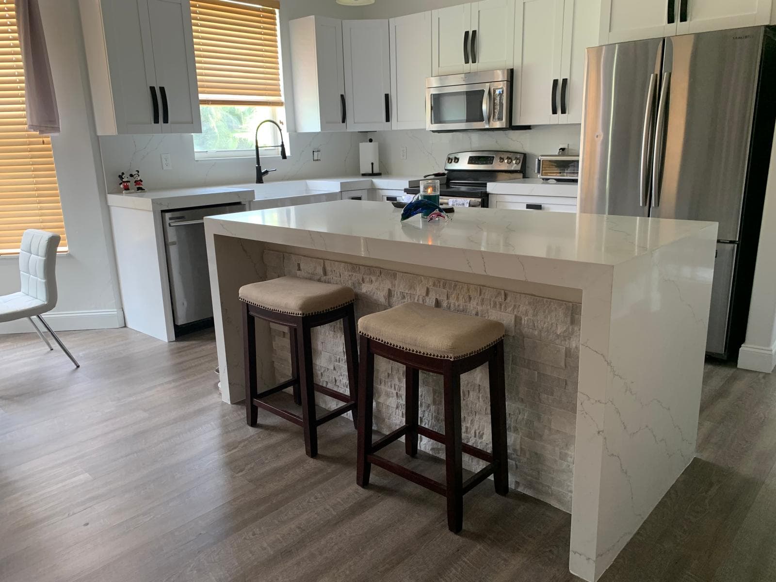White kitchen with quartz waterfall island and stone veneer base by Benito Fine Carpentry Wellington FL