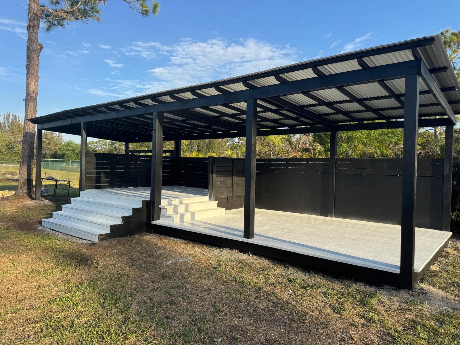 Large black metal-roof outdoor pavilion with white composite deck and privacy walls by Benito Fine Carpentry Wellington