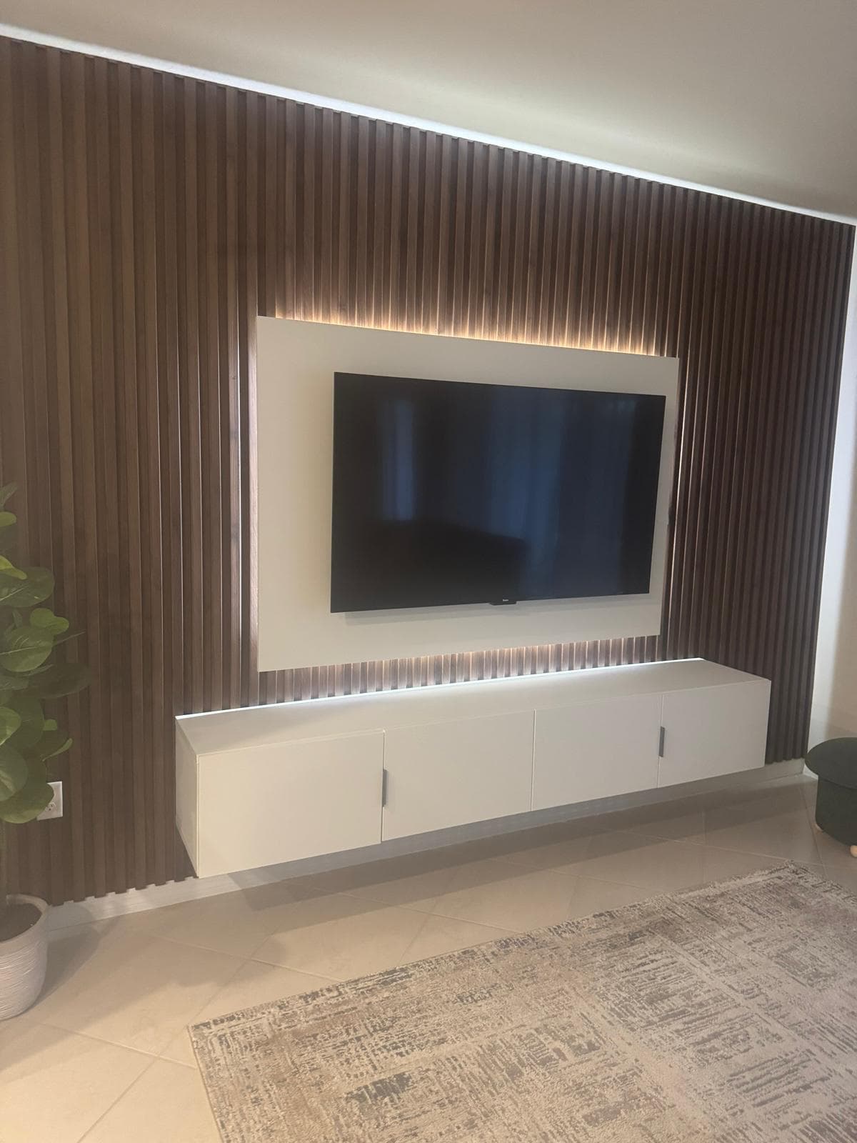 Dark walnut vertical slat accent wall with LED backlit TV and floating white media console — real client project by Benito Fine Carpentry