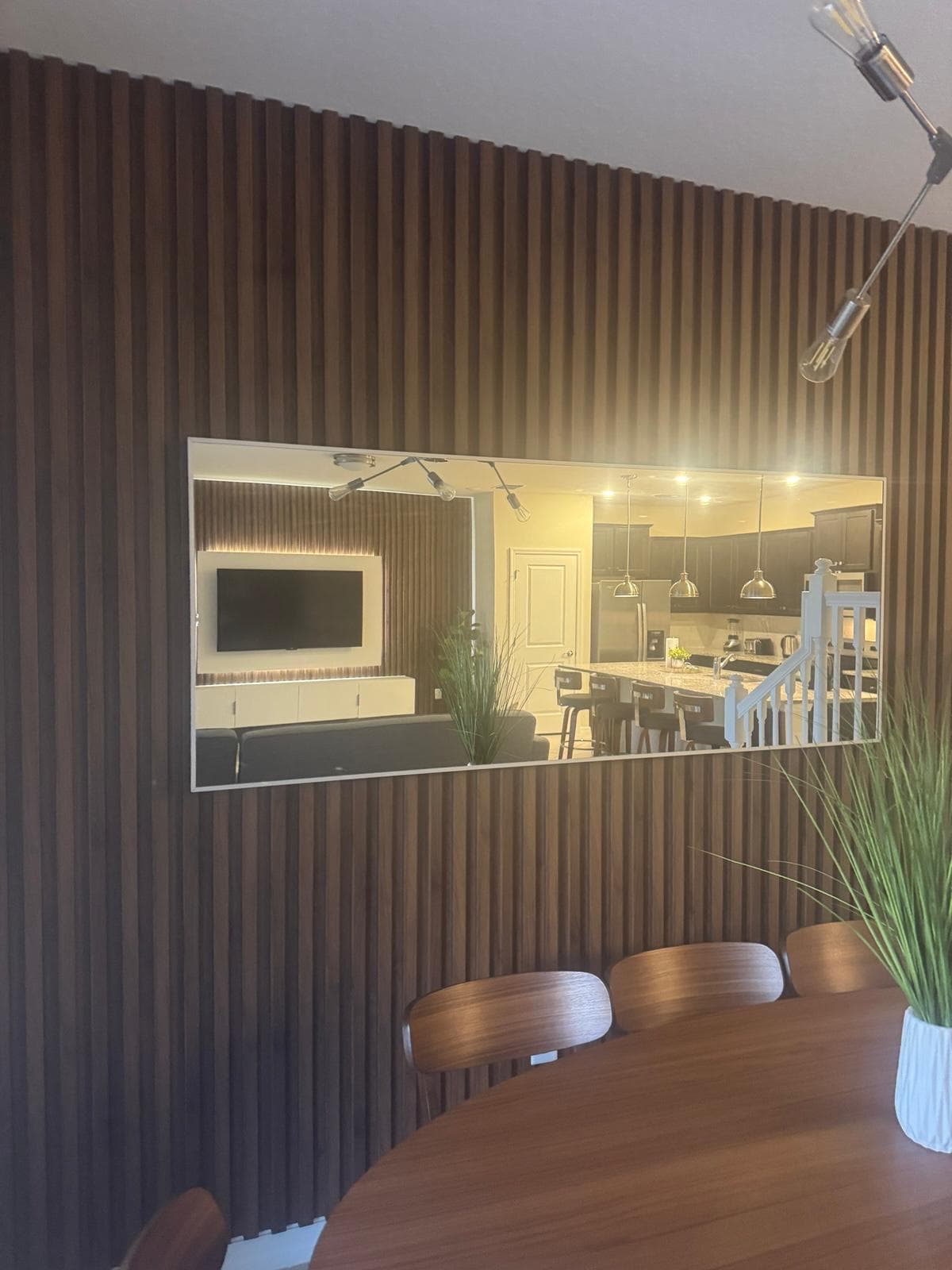 Dark walnut dining slat wall with mounted mirror reflecting open kitchen by Benito Fine Carpentry