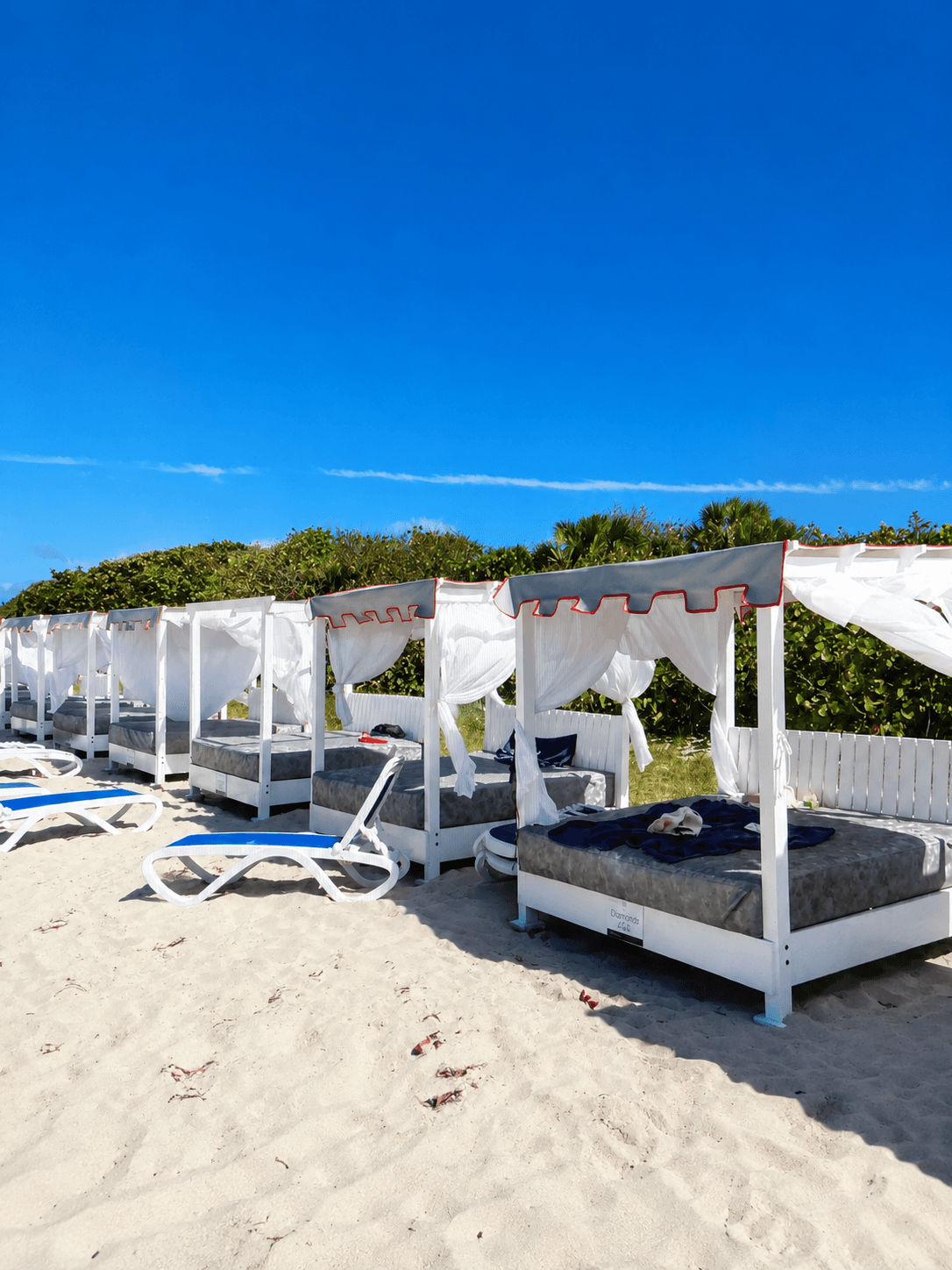 Custom white wood canopy beach cabanas with draped linen and day beds built by Benito Fine Carpentry