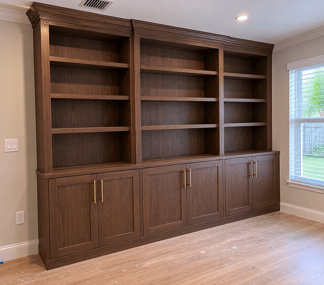 Custom dark walnut floor-to-ceiling built-in bookcase with brass pulls and crown molding by Benito Fine Carpentry Wellington