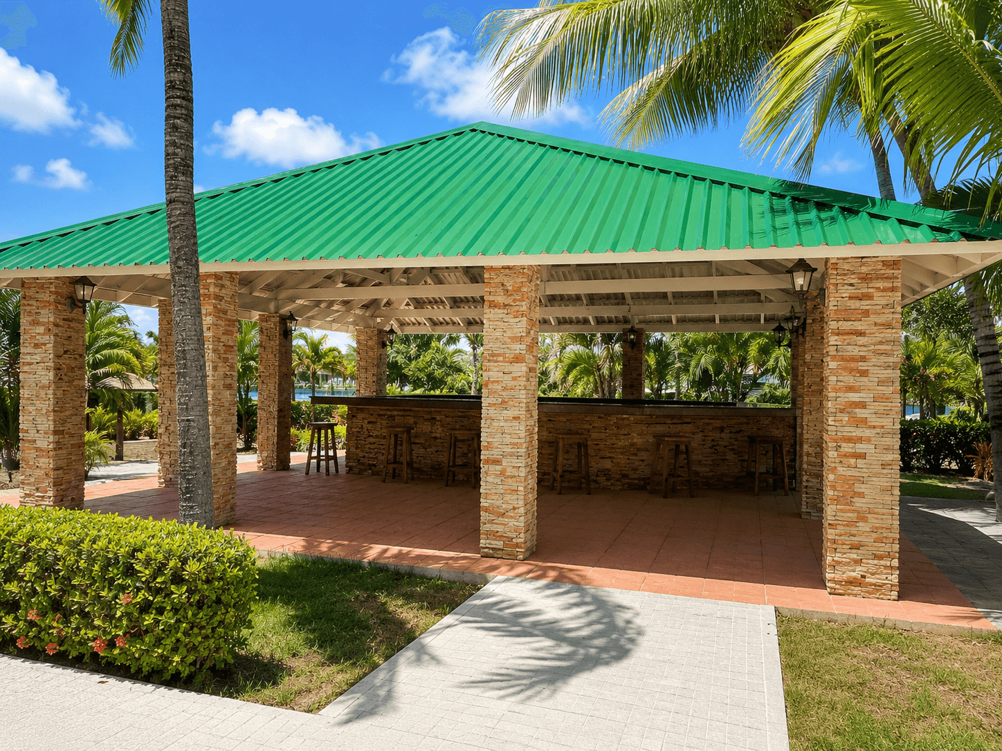Large open-air tropical pavilion with green corrugated metal roof and stone columns — hotel-grade structure