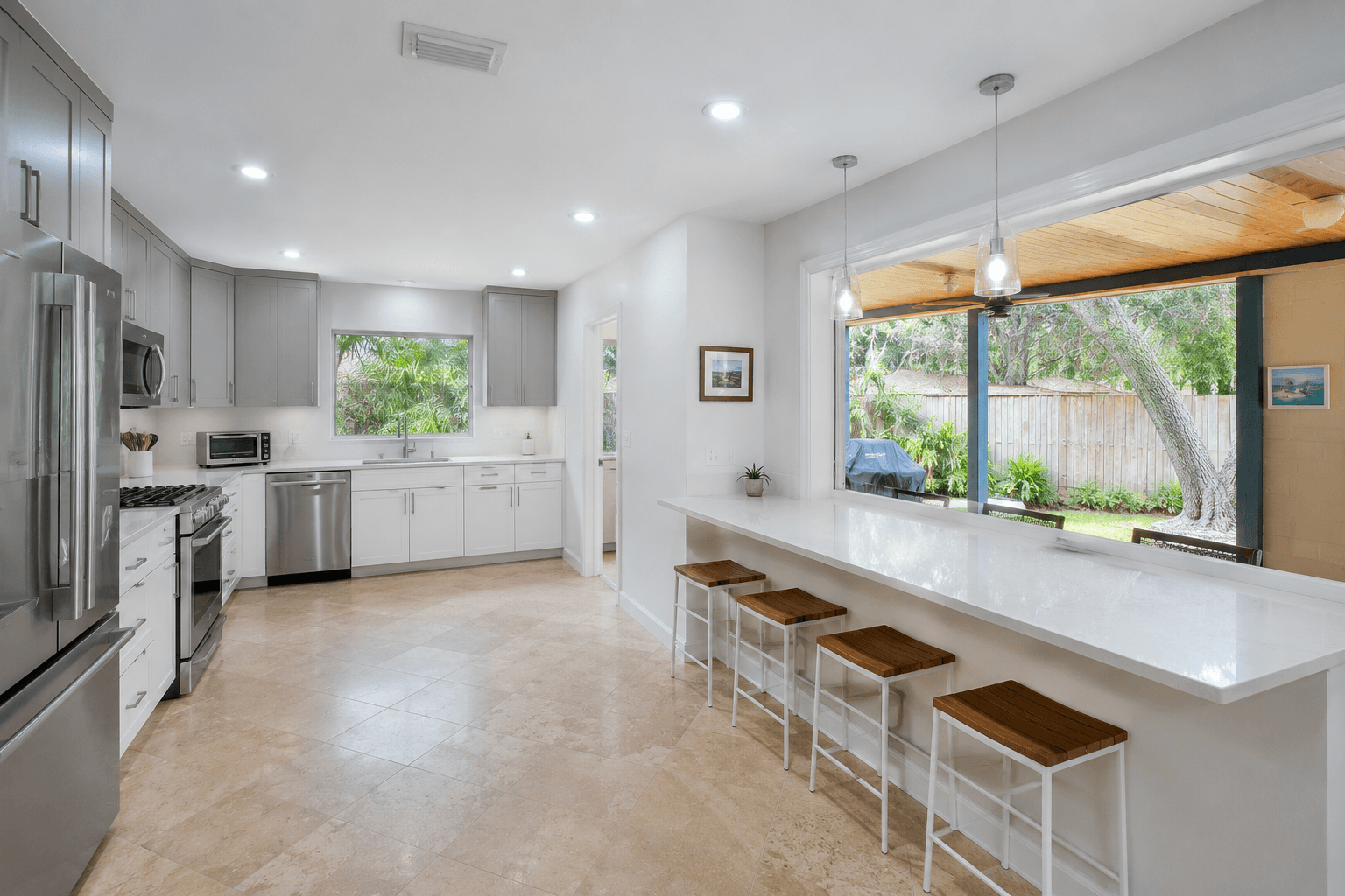 Open plan kitchen with pass-through window to covered patio travertine floor gray cabinets by Benito Fine Carpentry Palm Beach