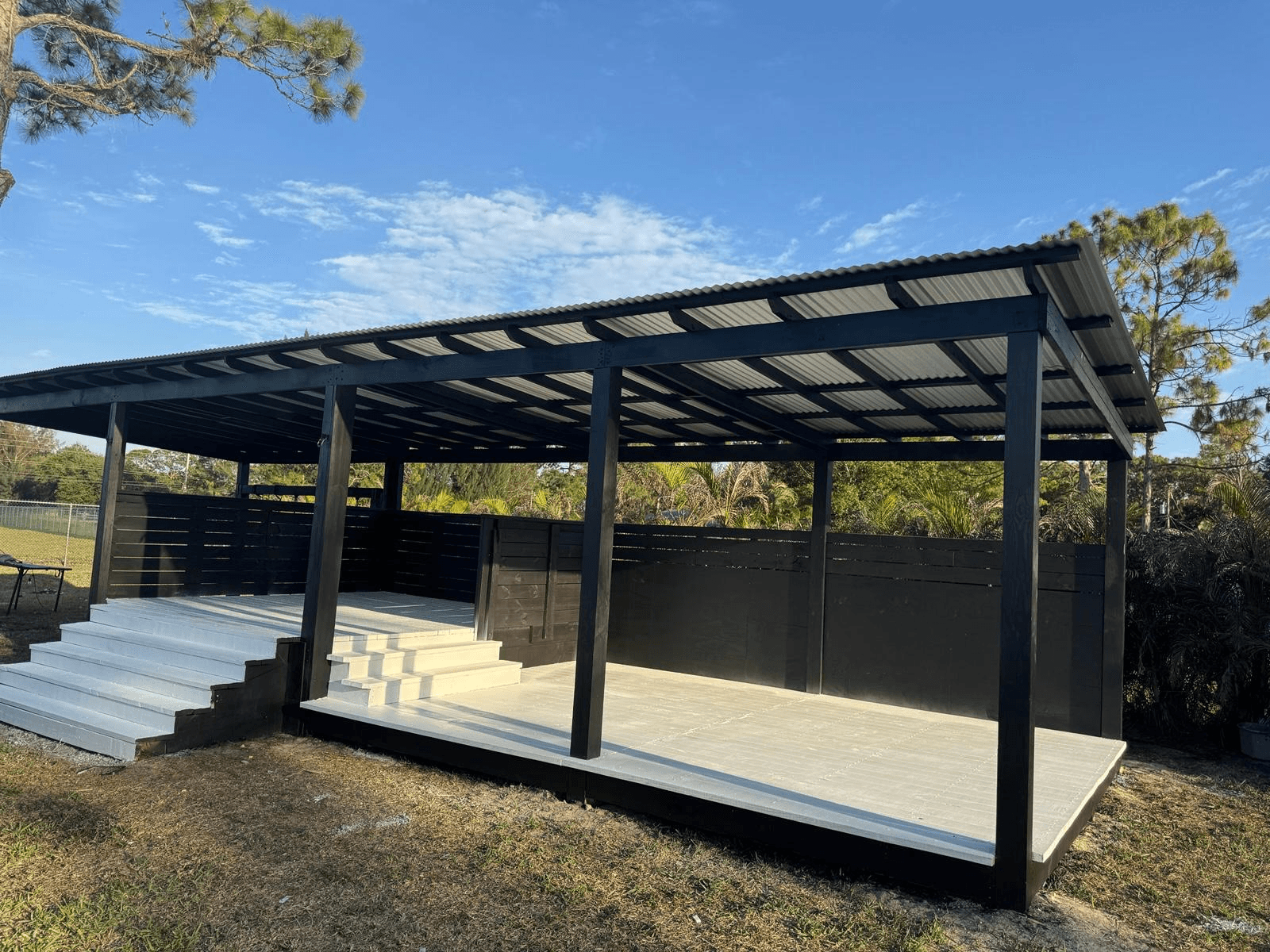 Modern black metal-roof outdoor pavilion with white concrete deck by Benito Fine Carpentry Wellington FL