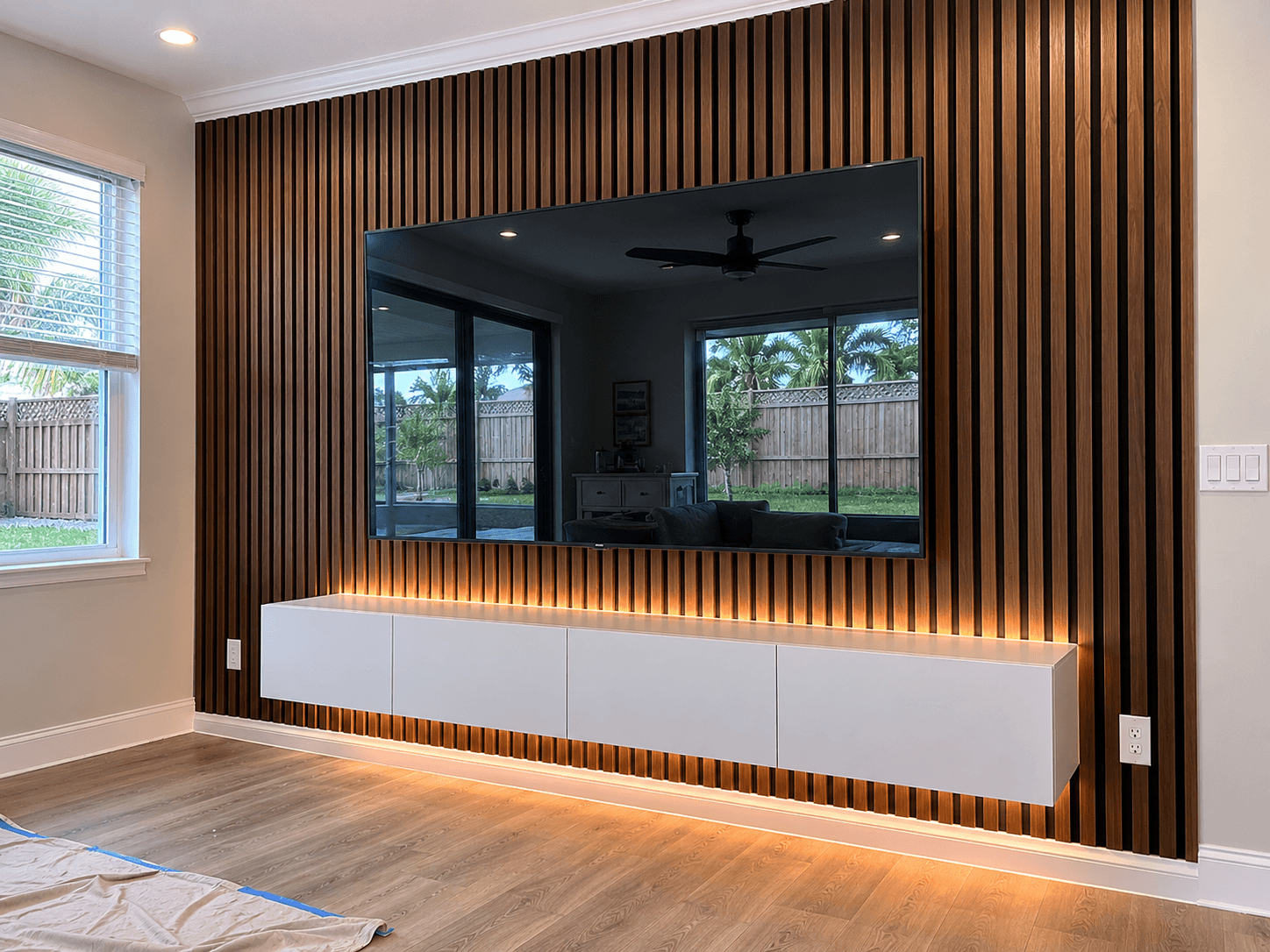 Dark walnut wood slat accent wall with LED strip floating white media cabinet mounted TV by Benito Fine Carpentry Palm Beach