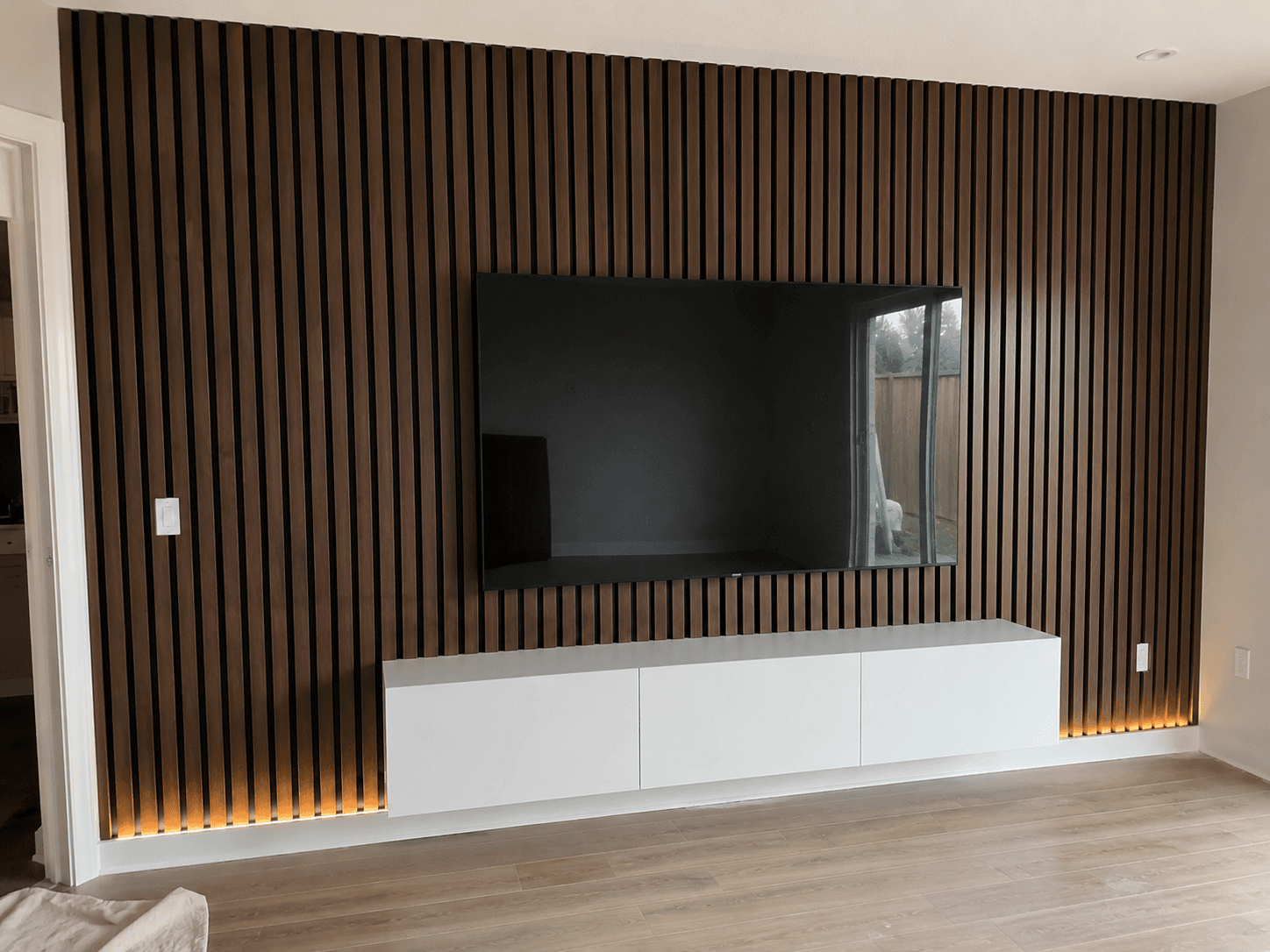Precision-spaced dark oak vertical slat wall with LED backlight and floating cabinet by Benito Fine Carpentry South Florida